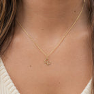 [group: w-10k-gold]A close-up of a person's neck and chest wearing a delicate gold chain necklace with a small lowercase 'c' initial pendant.