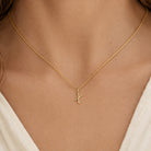 [group: x-10k-gold]A close-up of a model wearing a delicate gold chain necklace with a small, stylized gold pendant on a cream-colored top.