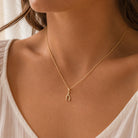 A close-up of a woman wearing a delicate gold chain necklace with a small gold horseshoe pendant, styled with a white top.