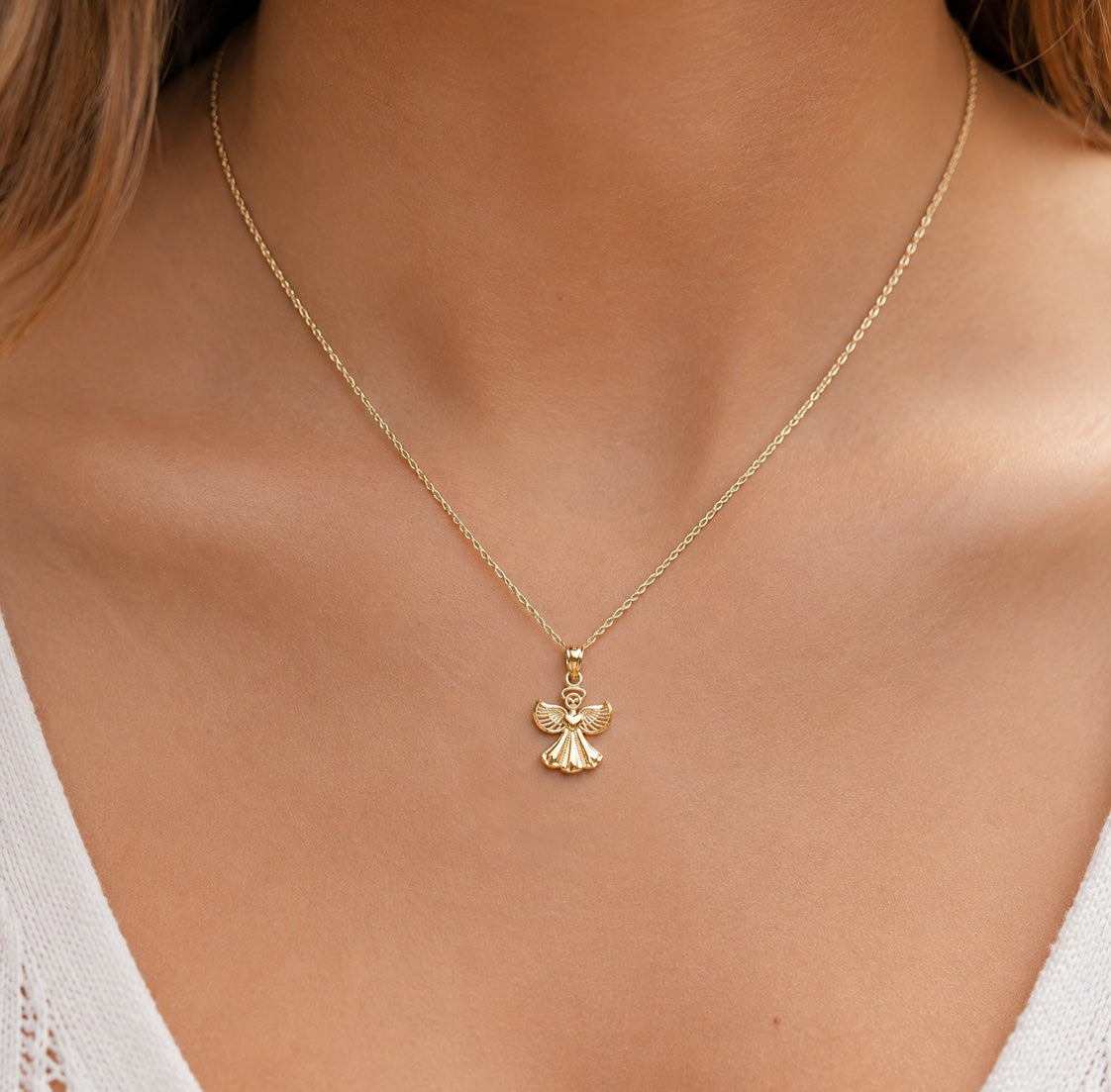 A delicate gold chain necklace with a small angel pendant, shown worn on a model's neck.