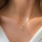 A delicate gold chain necklace with a small rose pendant featuring a light pink center, worn on a model's neck.
