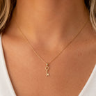 A delicate gold key pendant necklace with a heart-shaped key bow, worn on a model's neck over a white top.