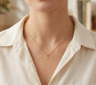 [group: small]A close-up of a person wearing a delicate gold chain necklace with a small crown pendant, styled with a cream-colored linen shirt.