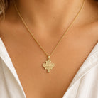 A gold necklace with a maple leaf pendant engraved with the word 'CANADA', worn by a model in a white top.