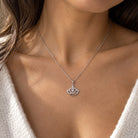 A close-up of a woman's neck and chest wearing a delicate silver chain necklace with a small crown-shaped pendant set with clear stones.