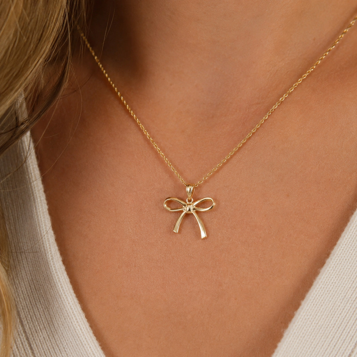 [group: 10k-gold-large] Gold necklace with a bow pendant on a person wearing a white top.