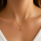 [group: gold-plated]A delicate gold chain necklace with an Om symbol pendant, shown worn on a model's neck over a white ribbed top.