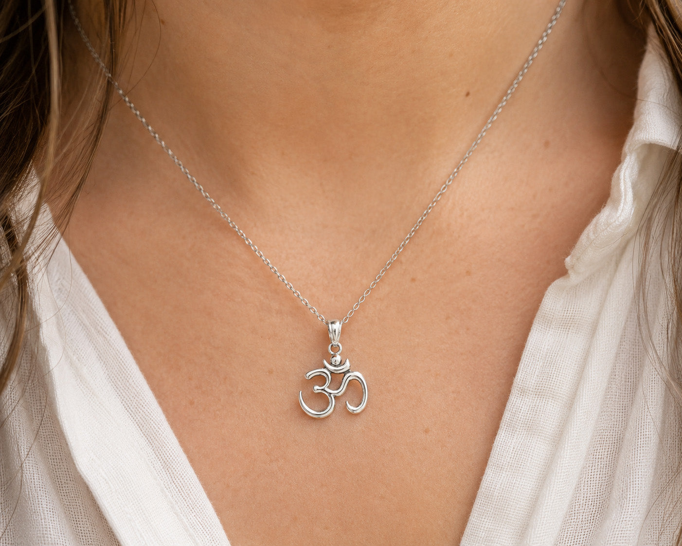 [group: silver]A sterling silver Om pendant necklace worn by a person, shown close-up against a white collared shirt.