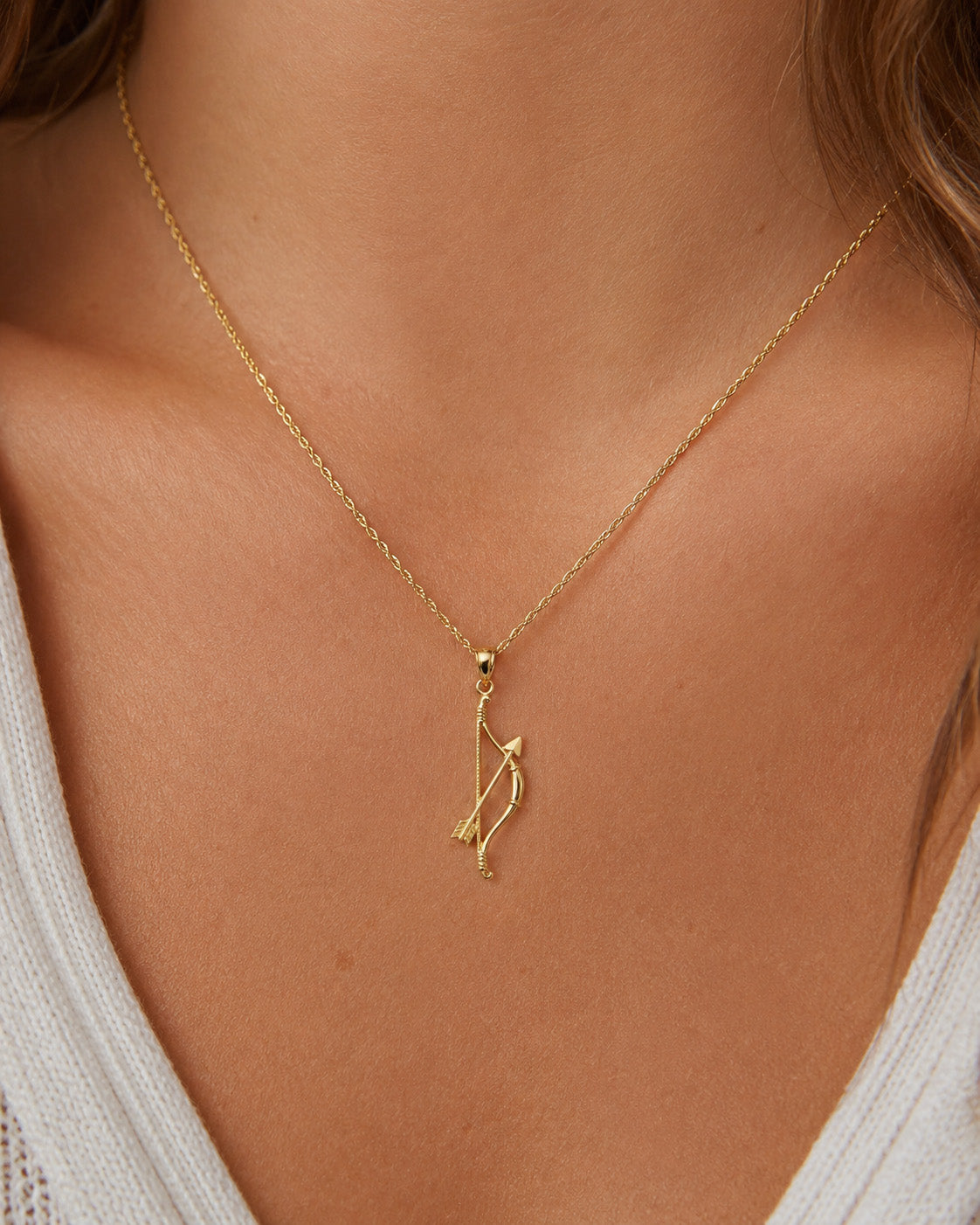 [group: large]A delicate gold chain necklace with a minimalist bow and arrow pendant, shown worn on a model's neck over a white knit top.