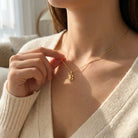 [group:10k-gold] Person wearing a gold necklace with a delicate pendant, set against a neutral indoor background.