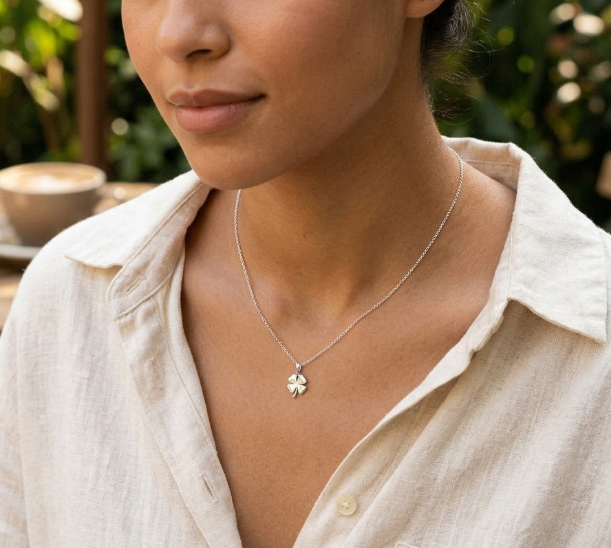 [group:silver] Person wearing a silver necklace with a clover pendant outdoors