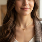 [group:10k-gold-small] Woman wearing a gold necklace with a bow pendant