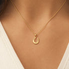 A close-up of a gold horseshoe pendant necklace worn on a model's neck, paired with a white ribbed V-neck top.