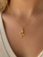 A close-up of a model wearing a delicate gold necklace with a rose-shaped pendant, styled with a beige knit top.