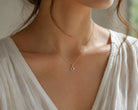 Close-up of a person wearing a delicate gold necklace with a small evil eye pendant.