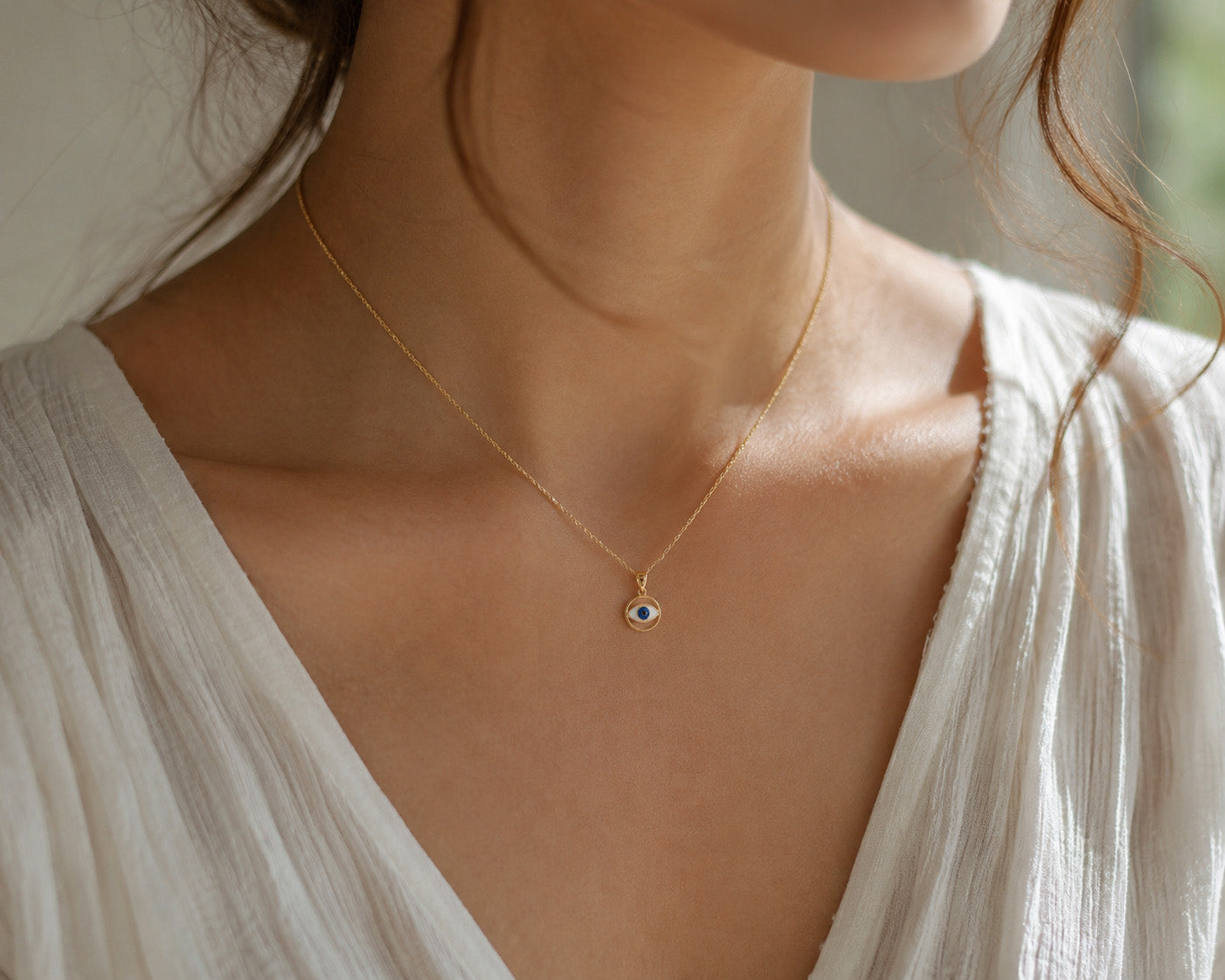 Close-up of a person wearing a delicate gold necklace with a small evil eye pendant.