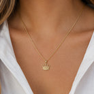 [group: large] A close-up of a model wearing a delicate gold chain necklace with a small crown pendant, styled with a white collared shirt.