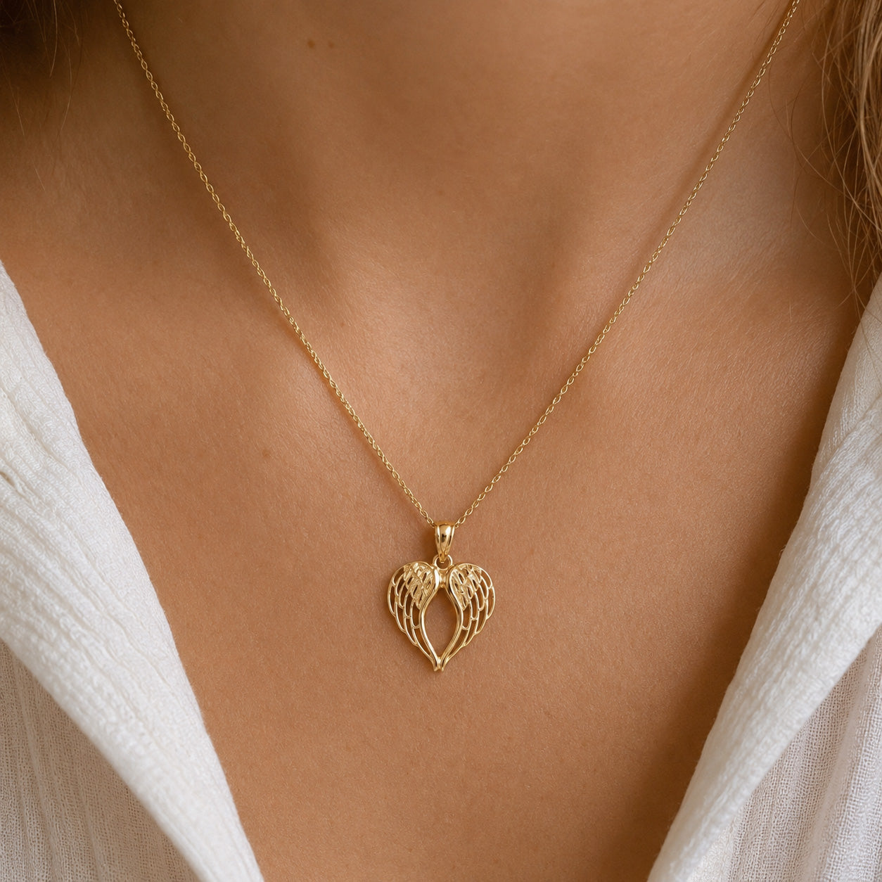[group: large]A delicate gold chain necklace with a textured, openwork heart-shaped pendant, shown worn on a model's neck over a white top.