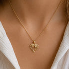 [group: large]A delicate gold chain necklace with a textured, openwork heart-shaped pendant, shown worn on a model's neck over a white top.