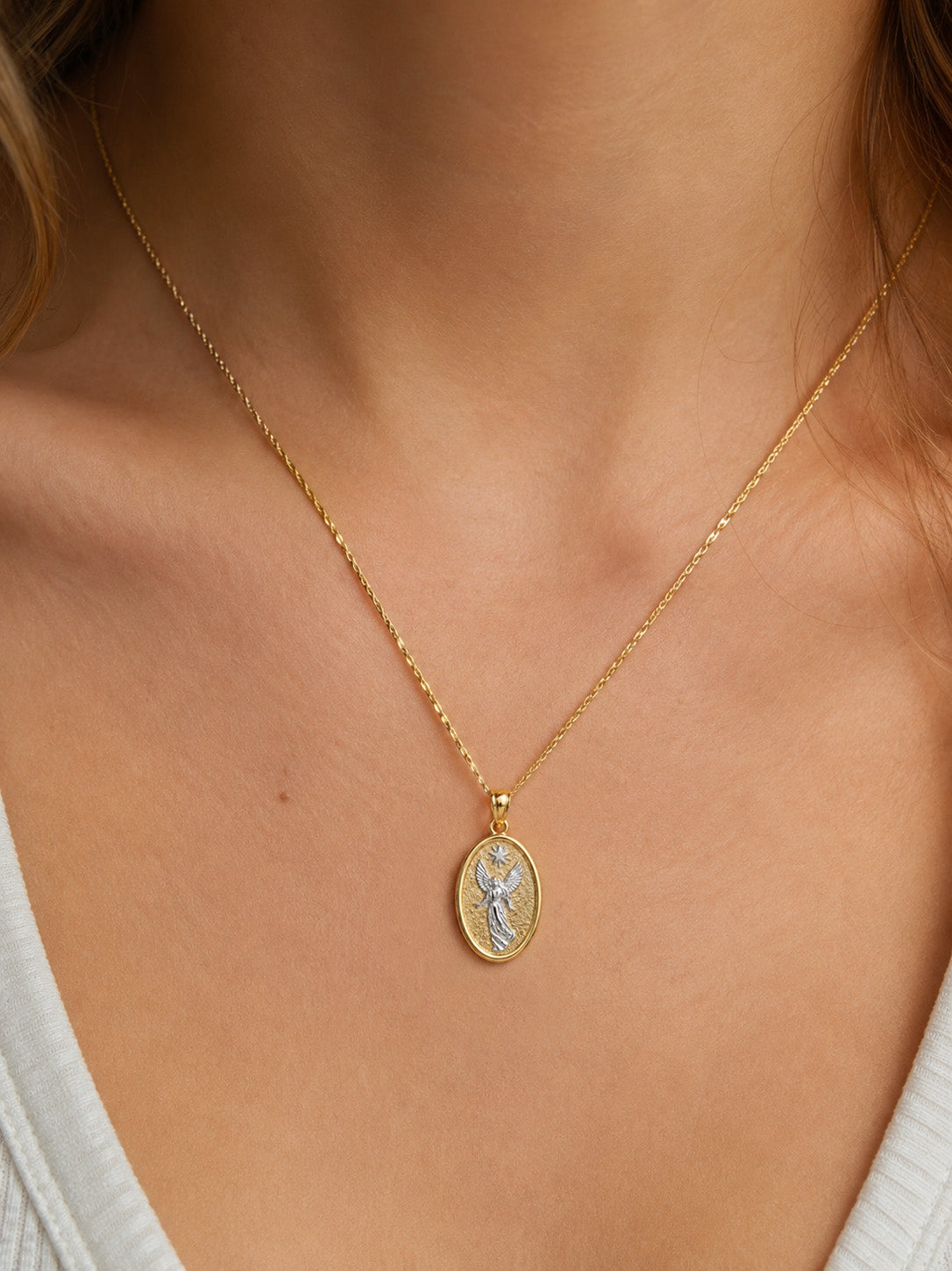 A gold chain necklace with an oval Saint Michael pendant, worn on the neck of a model.