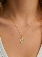 A gold chain necklace with an oval Saint Michael pendant, worn on the neck of a model.
