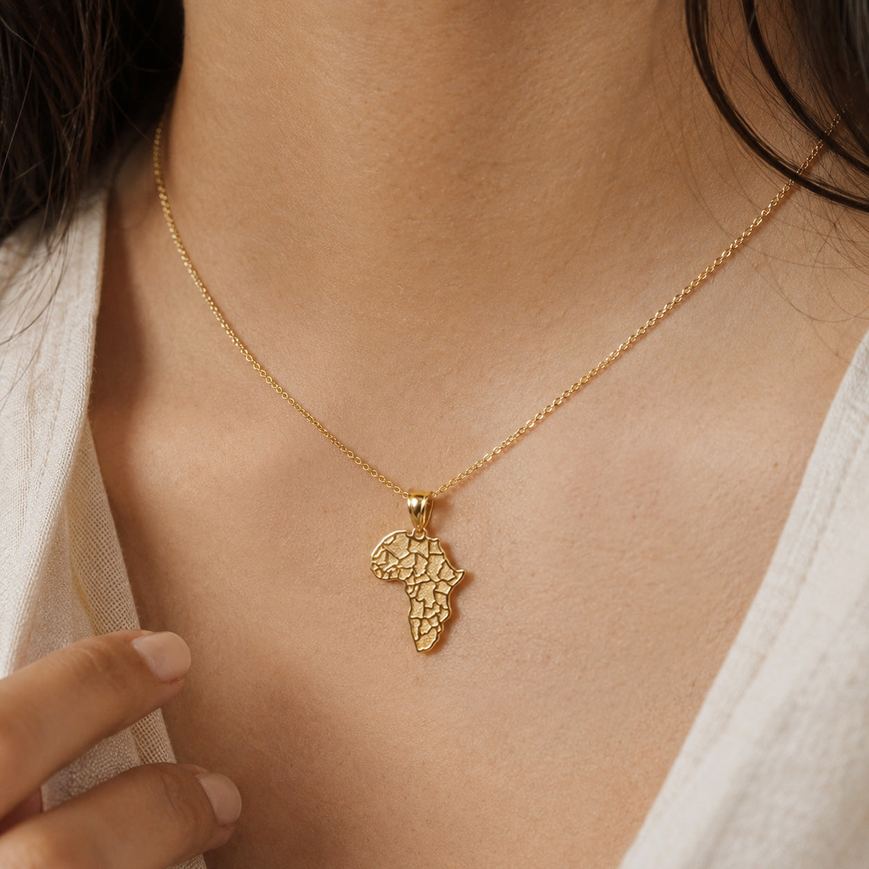 [group:gold-plated] Gold necklace with a map of Africa pendant on a person wearing a white shirt.