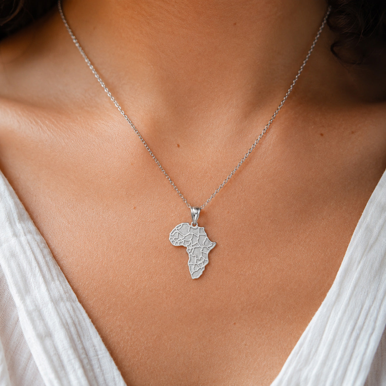 [group:silver] Silver necklace with an Africa map pendant on a person wearing a white top.