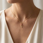 [group: small] Gold necklace with a rose pendant worn by a person in a white top.