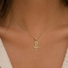 A delicate gold chain necklace with a rose-shaped pendant, worn by a model. The necklace is shown close-up against the model's neck and upper chest, with a cream-colored knit top visible at the edges.