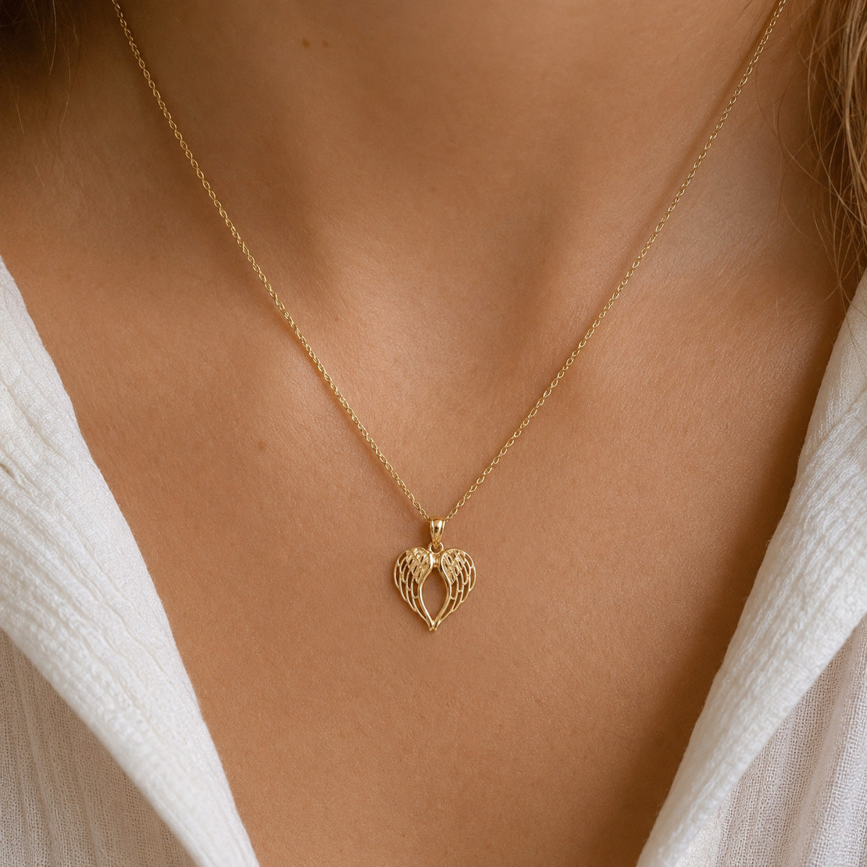 [group: small] A delicate gold chain necklace with a textured, openwork heart-shaped pendant, shown worn on a model's neck over a white top.