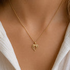 [group: small] A delicate gold chain necklace with a textured, openwork heart-shaped pendant, shown worn on a model's neck over a white top.