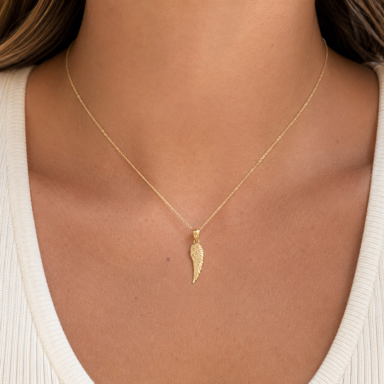 [group: small]A delicate gold chain necklace with a textured wing-shaped pendant, shown worn on a model's neck over a white ribbed top.