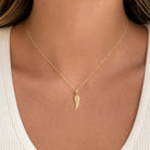 [group: small]A delicate gold chain necklace with a textured wing-shaped pendant, shown worn on a model's neck over a white ribbed top.