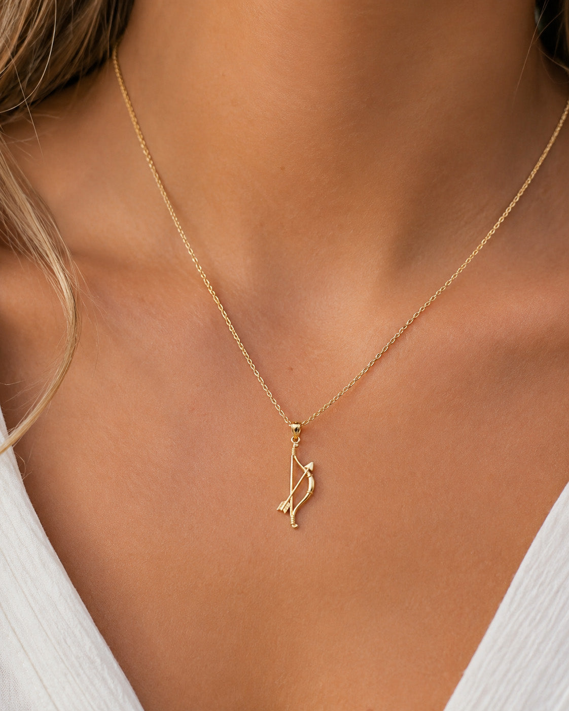 [group: small]A delicate gold chain necklace with a small bow and arrow pendant, shown worn on a model's neck.