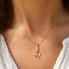 A close-up of a model wearing a delicate gold chain necklace with a small rose-shaped pendant, styled with a white knit top.