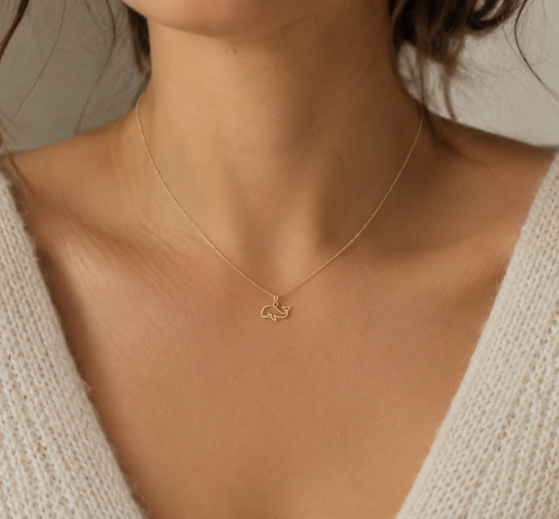 Gold necklace with a small pendant on a person wearing a beige sweater.