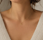 Gold necklace with a small pendant on a person wearing a beige sweater.
