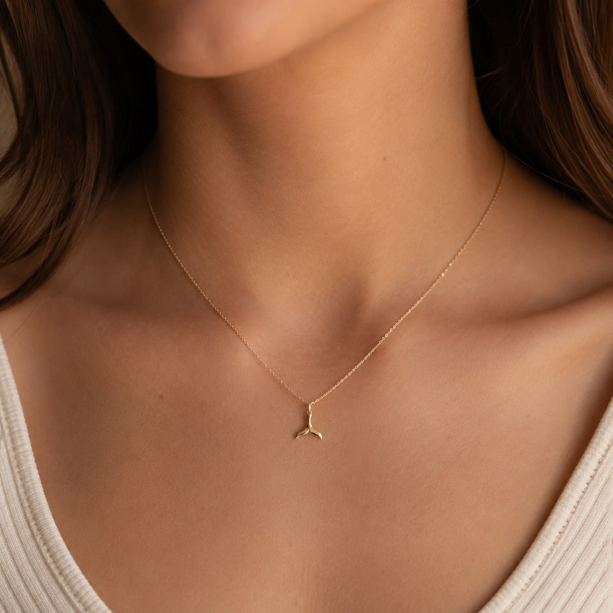 Gold necklace with a small pendant on a person wearing a white top.