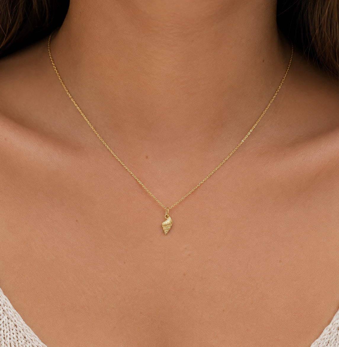 A delicate gold chain necklace with a small textured gold pendant, shown worn on a model's neck.