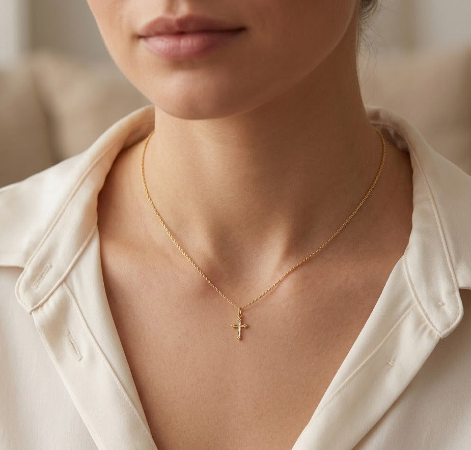 Close-up of a person wearing a gold necklace with a cross pendant.