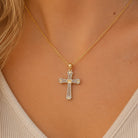 [group: gold-plated]A gold cross pendant necklace with small clear stones, worn on a model's neck over a light beige ribbed top.