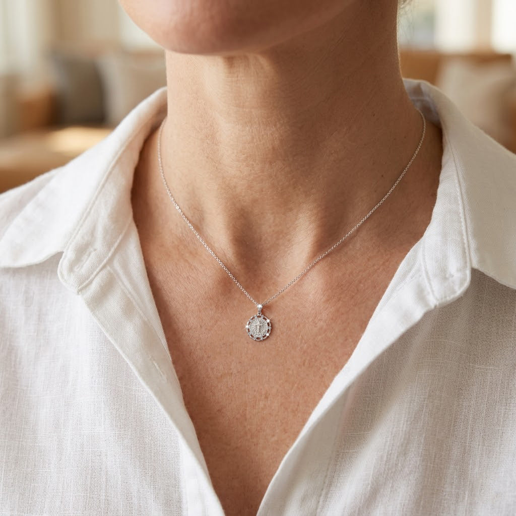 [group:silver] Person wearing a silver necklace with a pendant in a softly lit room.