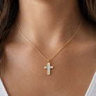 A gold cross pendant necklace with a light blue inlay, worn on the neck of a model.