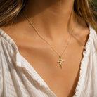 A delicate gold chain necklace with a small cross pendant worn by a model in warm natural light.