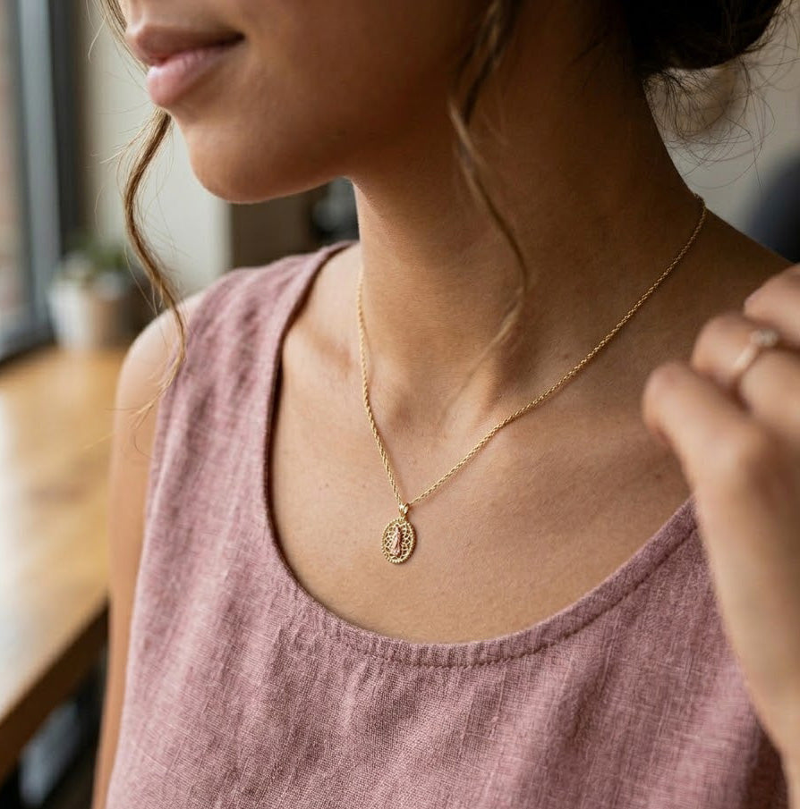 Woman wearing a Gold Guadalupe Pendant  with a pink top indoors