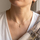 Close-up of a person wearing a gold necklace with a cross pendant, with a light colored  background.