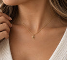 [group: 10k-gold-small] A close-up of a woman's neck and chest wearing a delicate gold chain necklace with a small gold pendant, paired with a white knit sweater.