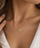 [group: small]A close-up of a model wearing a delicate gold chain necklace with a small oval pendant featuring a clear stone.