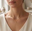 Gold necklace with a cross pendant on a person wearing a white top, blurred indoor background