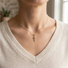 Person wearing a gold necklace with a cross pendant against a neutral background